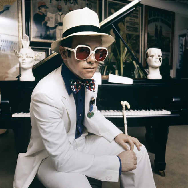 Elton John ao piano com óculos gigantes nos anos 70